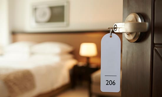 Hotel door open with room key hanging from doorknob with view of interior of hotel room. 